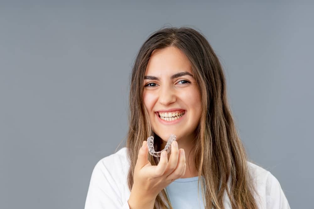 smiling girl holding a invisalign clear aligner